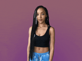 Video gif. Tinashe shrugs her shoulders as glances from side to side.