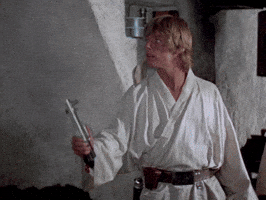 Star Wars gif. Mark Hamill as Luke Skywalker in Star Wars: Return of the Jedi holds a blue lightsaber in his hand. He looks at the lightsaber in awe as it lights up and flashes back down. 