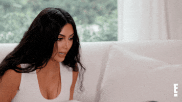 Reality TV gif. Kim Kardashian looks down in shock, then sits back with her hand over her mouth.