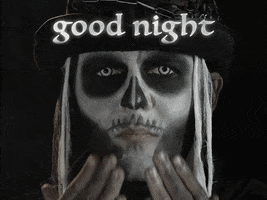 Video gif. Closeup of a man in skeleton makeup blowing a kiss with a cloud of smoke coming out of his mouth and obscuring his face as he gives a creepy smile. Goth-style text reads, "Good night."