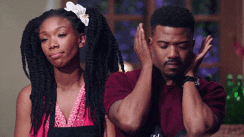 Reality TV gif. Brandi and Ray J stand next together. Brandi blankly stares with a disappointed look on her face. Ray J covers his face in shame.