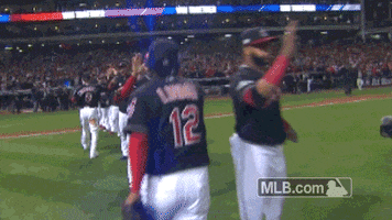 Sports gif. Cleveland Indians baseball player skips down a line of players on the field, giving them high fives.