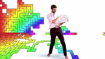 Video gif. Bearded man standing in a room full of rainbow mazes that are in the process of being coded holds a laptop and types indiscriminately into the keyboard as he looks at us and gives us a thumbs up. The word “awesome” spins in front of him.