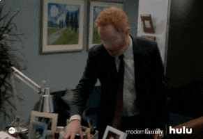 TV gif. Jesse Tyler Ferguson as Mitchell on Modern Family. He picks up his coffee mug and tries to leave but gets called back so he does a smooth 360 turn and leans his head in to listen.