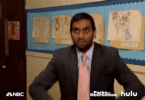 Parks and Recreation gif. Aziz Ansari as Tom looks at someone off screen and throws a bunch of dollar bills into the air. 