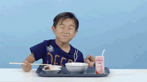 Asian child dancing in seat and smiling with eyes closed while eating desserts