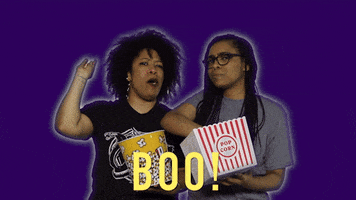 Celebrity gif. Against a dark blue background with glowing white outlines around themselves, Heben Nigatu and Tracy Clayton show they're not happy by booing and and throwing popcorn at us. Text, "Boo!"
