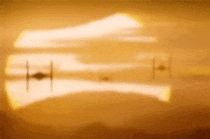 Movie gif. Three Tie Fighters from Star Wars: The Force Awakens closing in from the horizon, flying through a golden landscape as they ominously approach.
