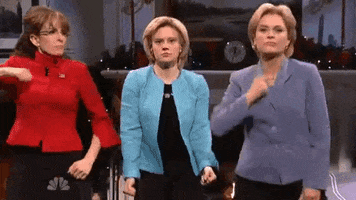 SNL gif. Tina Fey as Sarah Palin, Kate McKinnon as Hillary Clinton, and Amy Poehler as Hillary Clinton wear colored blazers as they dance in front of a fireplace with Christmas decorations.