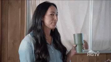 Reality TV gif. Joanna Gaines on Fixer Upper, holding a green travel coffee mug, makes eye contact with us and winks.