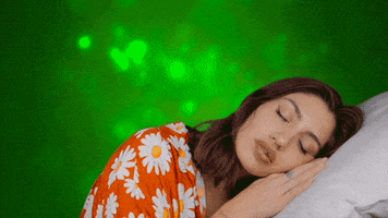 Video gif. Woman wearing an orange floral shirt is laying on a pillow with her hands folded under her head as she sleeps.