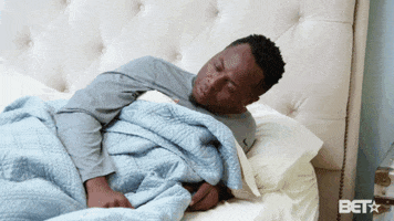 TV gif. Gene Harding on The Gary Owen's Show is cuddled up in bed with a blue blanket spread over himself, propped up on one elbow. He throws his head back as he listens tiredly.