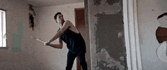 Music video gif. From video for Phantogram's You Don't Get Me High Anymore, a man in a semi-demolished room swings a hatchet through a wall.