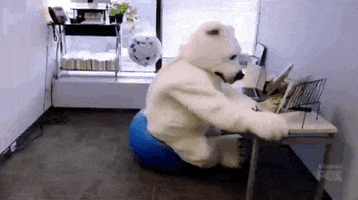 Video gif. A person dressed in a full body polar bear suit sits on an exercise ball at a desk. They lose their balance and fall, knocking papers and things off the desk, and cause a huge moment of chaos as we see the polar bear face plant in an office.