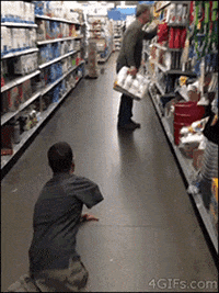 Video gif. A man with no legs is pranking a man in an aisle of a store. He marine crawls over to the man peering at the shelf and scares him, making the man jump away and throw his toilet paper at the man on the floor.