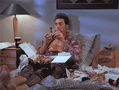 Seinfeld gif. Michael Richards as Kramer sitting in bed, tapping his feet, and contentedly chowing down on a box of fried chicken.