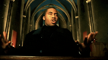 Music video gif. From the Got Yourself A Gun video: sitting in a pew inside of an ornate church, rapper Nas prays and sings with feeling.
