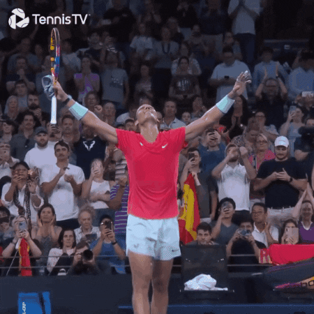 Sports gif. Rafael Nadal holds a tennis racket in one hand and has his head tossed back in elation. He outstretches both arms in celebration as he walks off the court.