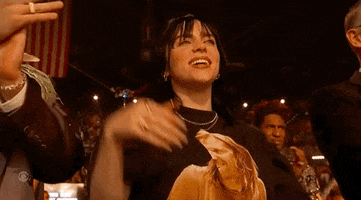 Celebrity gif. Billie Eilish is in the audience for the Grammys. She shakes her fists in the air and screams, “Yes!”