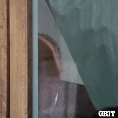 Movie gif. From a western movie on Grit TV, a man pulls back a curtain and nervously peers out of a window.