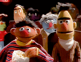Muppets gif. Bert and Ernie from Sesame Street sit in a crowded theater. Bert’s eyes are wide, riveted to the show while Ernie casually chomps on popcorn.