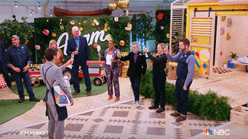 Reality TV gif. Camera pans around the set of Making It, where contestants and hosts raises their glasses to cheers and clap their hands.