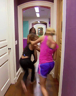 Reality TV gif. In a hallway, two women are fighting, and a third tries to pull one of them away while the other continues reaching and slapping, while the production crew peeks out from the corner..