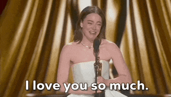 Oscars 2024 GIF. Emma Stone clutches her trophy in one hand and uses hand motions to punctuate her statement, as she says, "I love you so much."