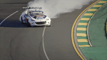 Sports gif. Racecar drifts around the steep curve of a track kicking up a trail of dust.