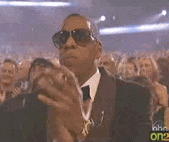 Celebrity gif. Jay-Z among a large audience, clapping his hands along with the others.