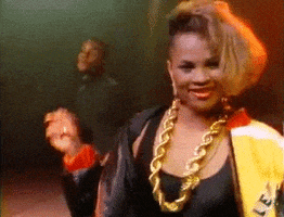 Music video gif. From the video for Push It, Salt dances on stage smiling at us, wearing a big bomber jacket, thick gold earrings and a gold chain.