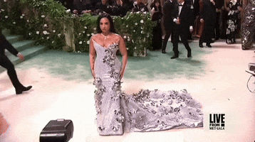Met Gala 2024 gif. Demi Lovato poses for the cameras turning side to side wearing a smokey lavender Pabral Gurung gown embellished with silver flowers, as we zoom in to see her stiffly toss her hair.