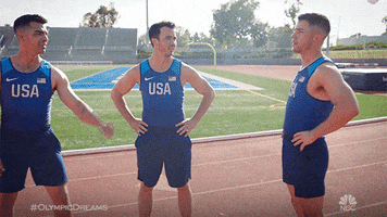 Celebrity gif. The Jonas Brothers stand on a running track in Olympic Team USA uniforms. They fist pump each other. 