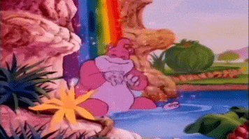 Cartoon gif. Wooly What’s-It in Adventures of Teddy Ruxpin sits under a rainbow waterfall and happily lets it wash over him.