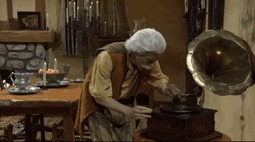 SNL gif. In an old-timey dining room with a fire in the fireplace, Willem Dafoe dances to music from a phonograph, wearing a white wig and moustache and a brown vest. 