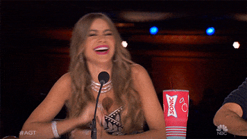 Reality TV gif. Sofia Vergara on America's Got Talent laughs as she leans to the side and rests her face on her forearms.