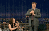 Late Night gif. Paget Brewster rises into an emphatic standing ovation as Conan O'Brien stands and salutes.