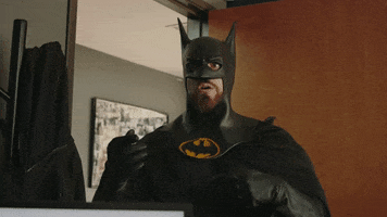Video gif. Man dressed as Batman is standing in an office and claps his hands in anticipation before punches his arm upwards, looking determined. He turns and walks out the door, with his cape swooshing behind him.