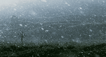Video gif. Snow falls heavily on a hilly landscape.