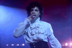 Celebrity gif. Prince dances onstage, licking his finger and then smoothing back his curly hair.
