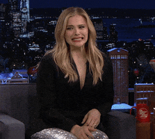 Celebrity gif. A guest on The Tonight Show, Chloë Grace Moretz laughs and shakes her head in disbelief, then covers her face with her hand.
