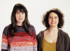 Celebrity gif. Abbi Jacobson and Ilana Glazer high five above their heads, then lower their hands to look at us with smiles.