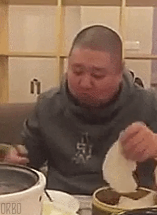 Video gif. A man picks up rice paper and hangs it in front of his mouth. He then picks up meat with his chopsticks and pushes the meat into the rice paper and then further into his mouth as the paper wraps around it. He does this continuously, over and over again. 