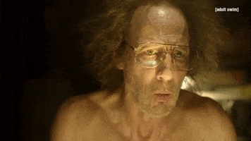 TV gif. A scene from Dream Corp LLC. A man with gray frizzy hair and aviator glasses stands without his shirt on. He has a surprised and relieved expression on his face. He says, “We're back.”