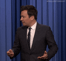 Tonight Show gif. Jimmy turns up his hands in mildly frustrated confusion. Text, "What."