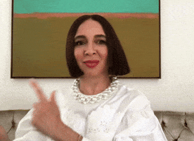 Celebrity gif. Maya Rudolph does a little dance as she sits. She points with her fingers and shimmies her shoulders to each side. Her blunt bob haircut shimmies with her. She then ends her little dance with her hands spreading out in a rainbow motion.