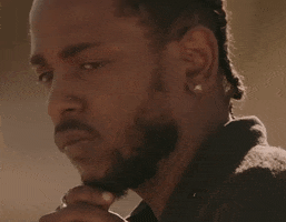 Celebrity gif. Kendrick Lamar looks over his shoulder, pensively stroking his goatee.