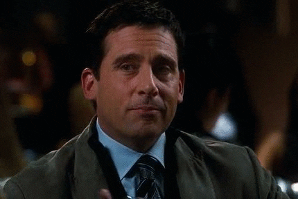 The Office gif. Steve Carell as Michael Scott lifts an alcoholic drink up, points to someone, and winks suavely. 