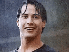 Celebrity gif. A young Keanu Reeves stands in the rain smiling. He raises up his arm and gives an enthusiastic thumbs up.