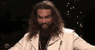 SNL gif. Jason Momoa smiles devilishly while looking around and holding out his arms.